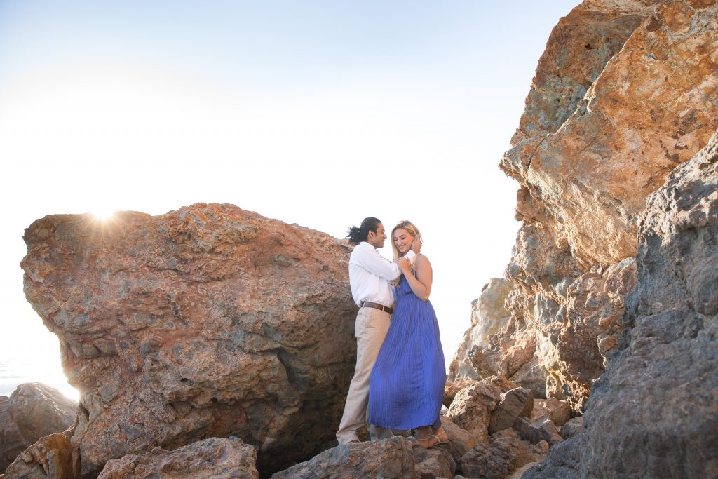 couple embrace inbetween rocks at beach proposal