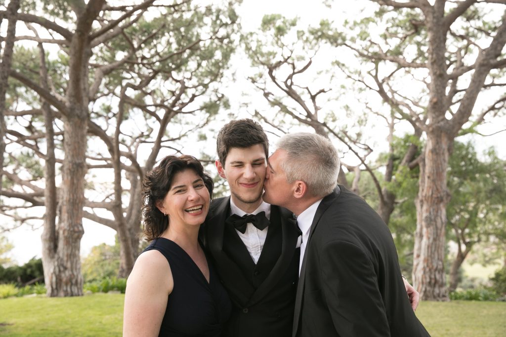 mom and dad kiss groom on wedding day