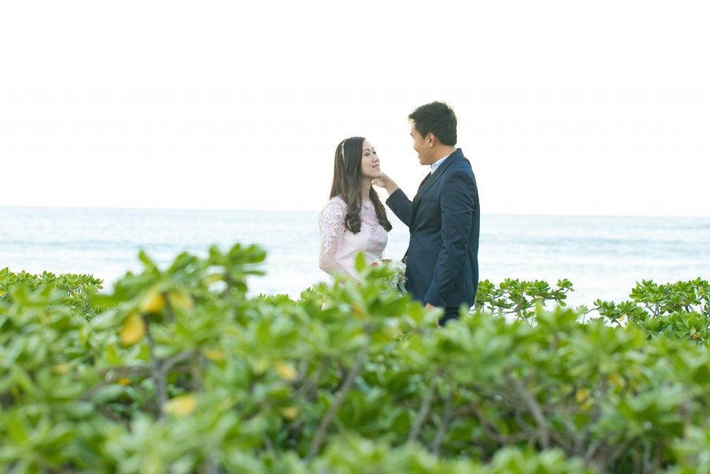 couple embrace on beach with greenery