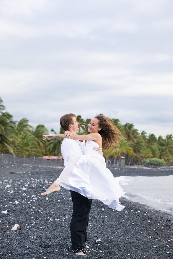 groom picks up bride and spins her around on black sand beach in wedding dress