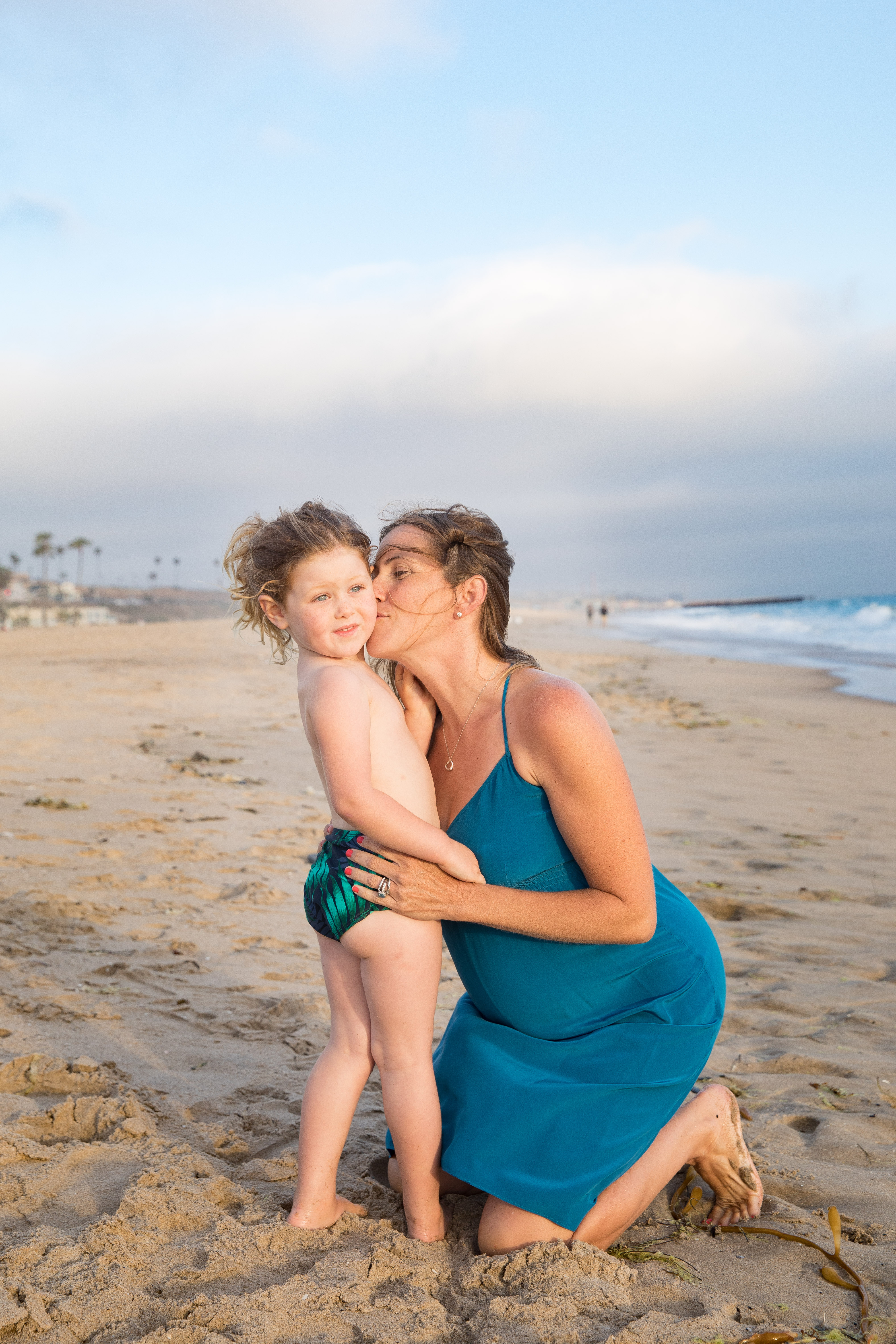 mom kisses toddler on beach while pregnant