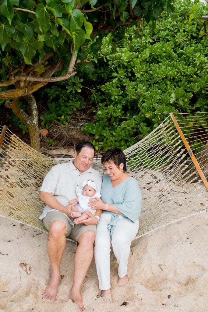 grandparents hold baby on hammock on the beach